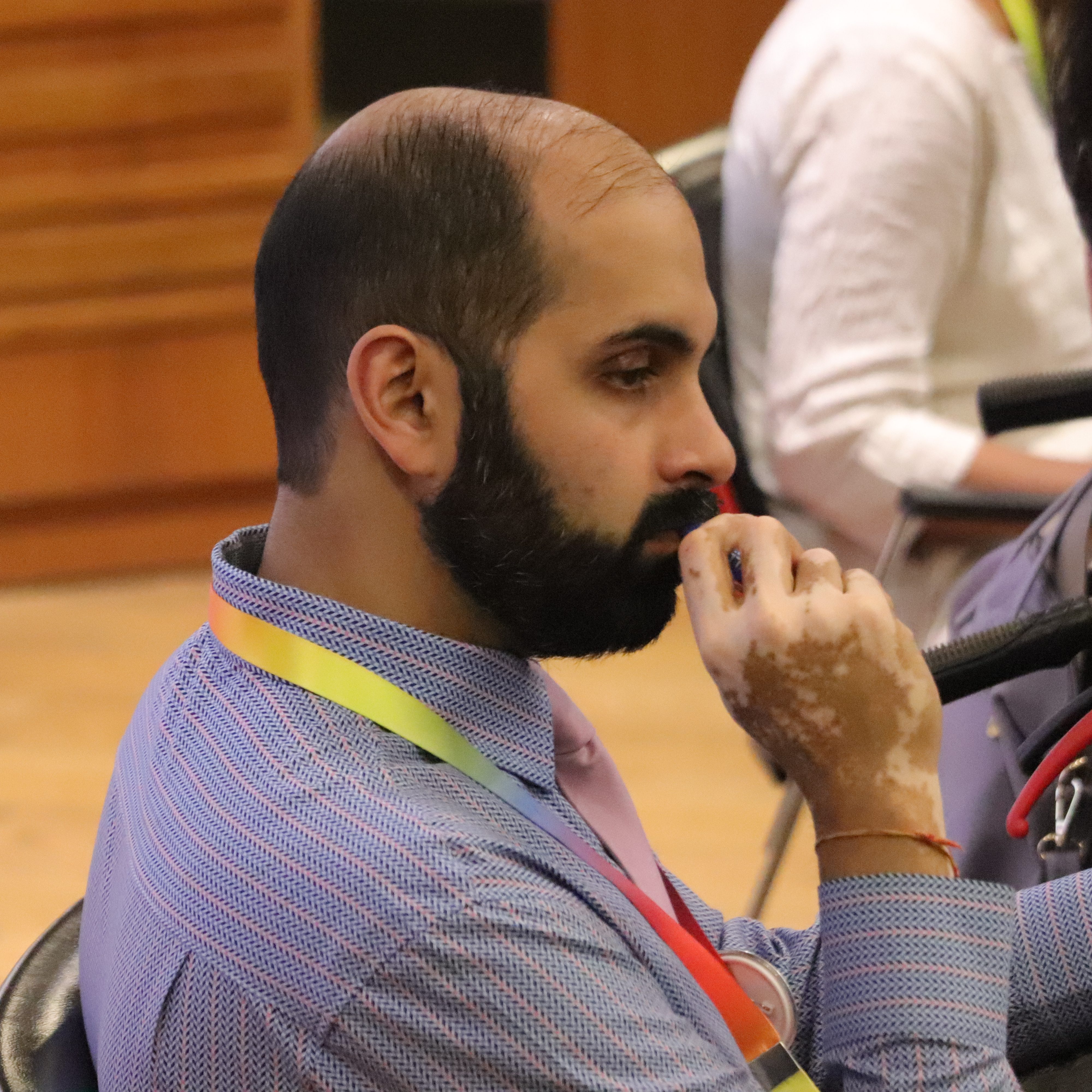 Anu Hazra, a bearded and balding brown-skinned man, with some pigment loss on the skin of his hands, wearing a lilac patterned shirt, sitting pensively